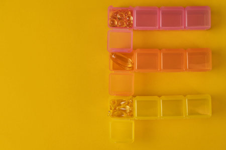 Multicolored organizers with yellow Omega 3 or vitamin D capsules on a yellow background with space...