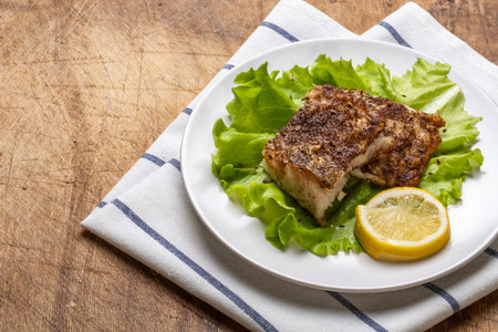 Two pieces of grilled fish fillet with the fresh leafs of lettuce and lemon on old wooden