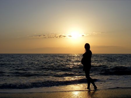 Silhouette of a pregnant girl on the background of a calm sea at sunsetの写真素材