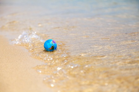 mini globe on the beach washed by wavesの写真素材