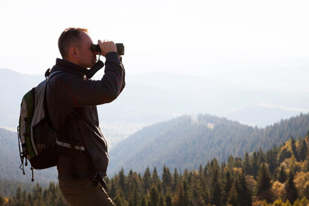 Hiker with backpack and binoculars looking at the mountains.