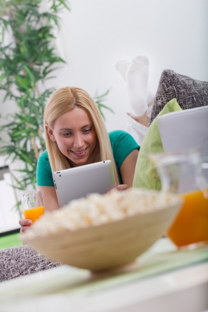 Young beautiful modern girl lying in sofa with electronic tablet の写真素材