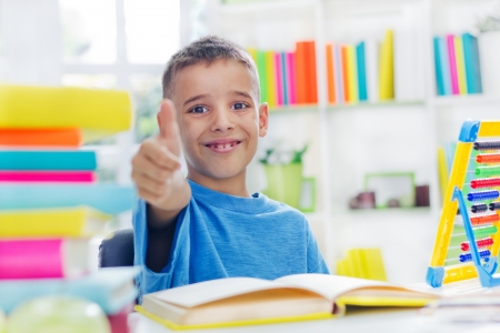 little school boy with thumb up doing homeworkの写真素材