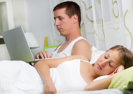 Couple with laptop in bed, Man using computer, woman sleepの写真素材