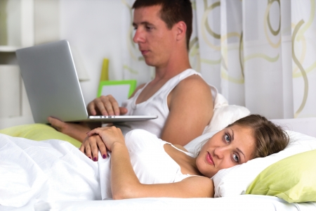 Couple with laptop in bed, Man using computer, woman upset and angryの写真素材