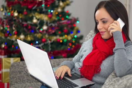 Smiling young woman with laptop sitting near Christmas tree の写真素材