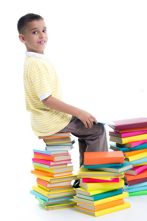 boy sitting on a pile of books and holding one book in his hands の写真素材
