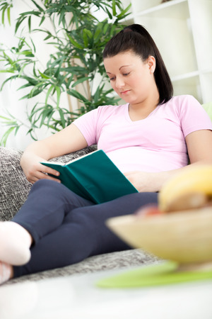  Pregnant woman lying on a sofa and reading a bookの写真素材