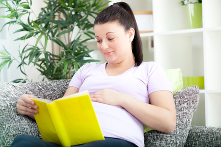 Pregnant woman lying on a sofa and reading a bookの写真素材