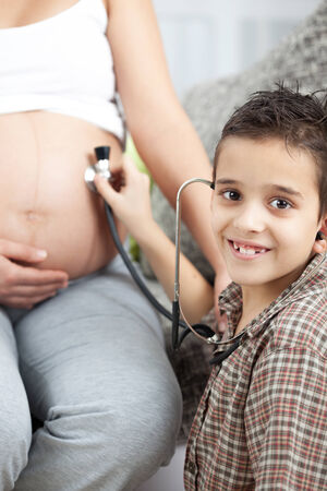 A little boy listens to a stethoscope belly of his pregnant mom の写真素材