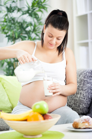 Pregnant woman sitting on the sofa, pour milk into a glassの写真素材
