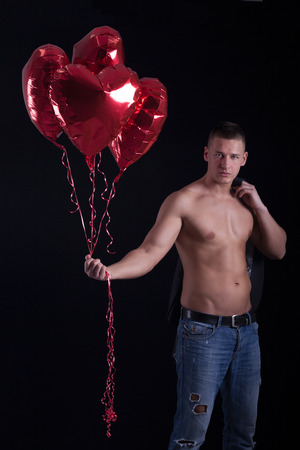 muscular young man holding a heart shaped balloon against black backgroundの写真素材