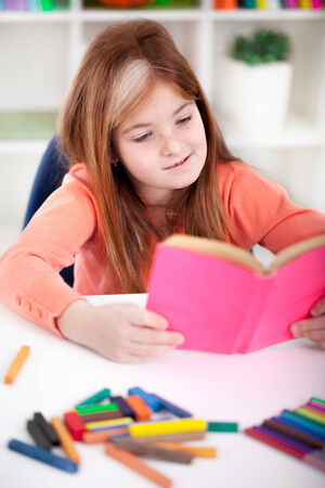 cute little red-haired girl reading a book at homeの写真素材