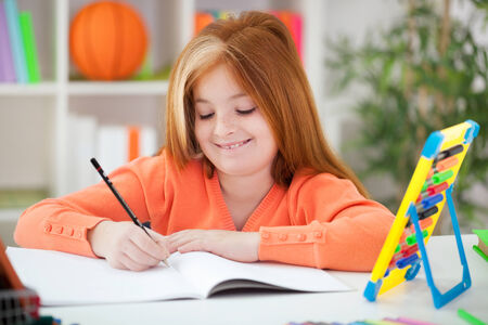 smiling red-haired girl doing her homework at homeの写真素材