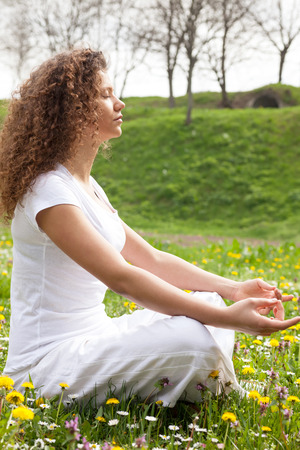 Young girl in lotus pose in the vild flower fieldの写真素材