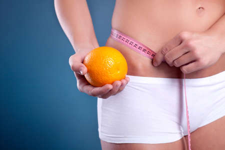  girl measures figure with a measuring tape and holding the orangeの写真素材
