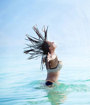 Woman splashing water with her hair in the seaの写真素材