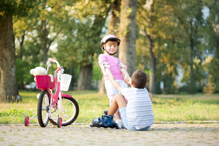 girl in park, helps boy with roller skates to stand up の写真素材