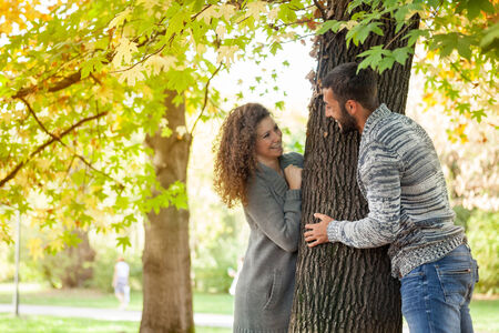 couple peeking from behind a tree  beautiful golden autumn season, love conceptの写真素材