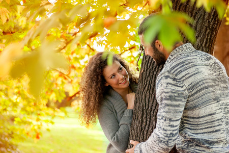 couple peeking from behind a tree  beautiful golden autumn season, love conceptの写真素材