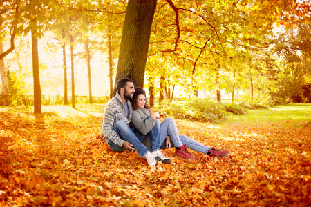 happy young couple leaning against a tree enjoying the autumn in parkの写真素材