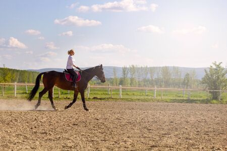 smiling blonde woman riding her brown horseの写真素材