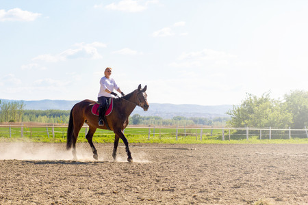 smiling blonde woman riding her brown horseの写真素材