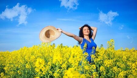 Attractive woman with outstretched arms in rapeseed field in summerの写真素材