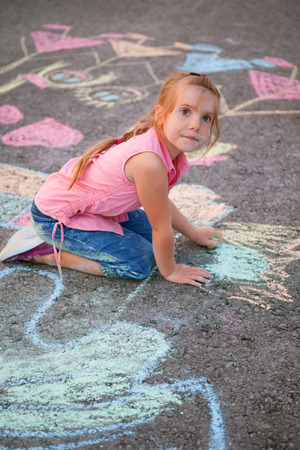 blonde little girl drawing with chalk on asphaltの写真素材