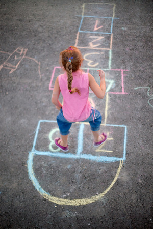 Cute blonde girl playing hopscotch on the streetの写真素材