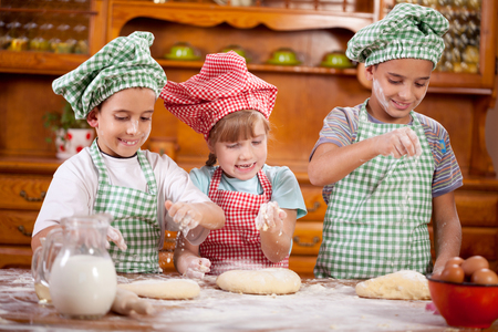 Three smiling child preparing dough for cookies in the kitchenの写真素材