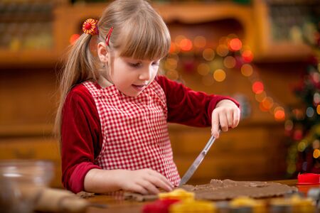 Happy young girl baking in kitchen Christmas cakes,Christmas tree in the backgroundの写真素材