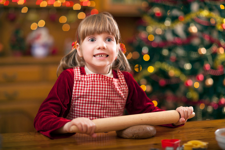 Happy young girl baking in kitchen Christmas cakes,Christmas tree in the backgroundの写真素材