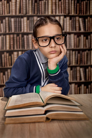 cute little boy is wearing eye glasses and reading a library book, education or learning conceptの写真素材