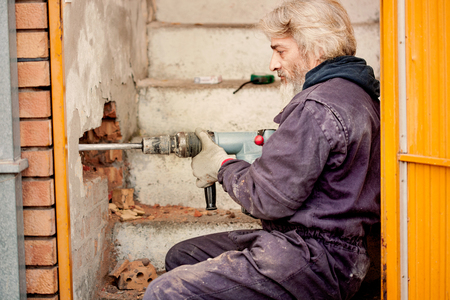 worker with pneumatic hammer drill perforator equipment making hole in wall at construction siteの写真素材