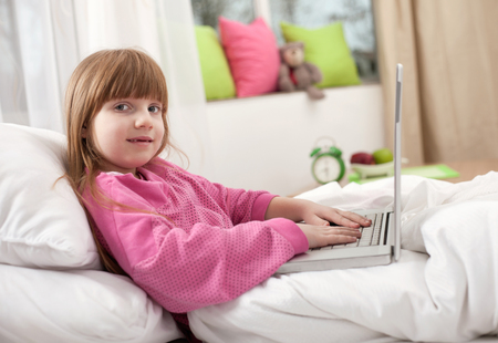 6 years old child having fun using laptop at her bedroomの写真素材