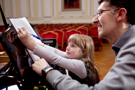 father teaches young daughter playing pianoの写真素材