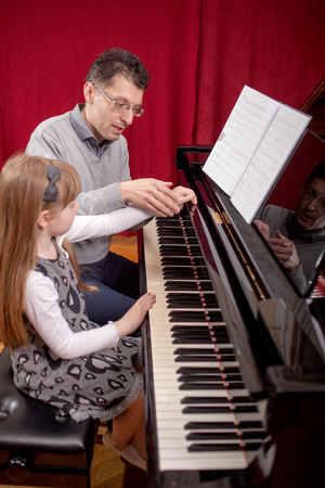 father teaches young daughter playing pianoの写真素材
