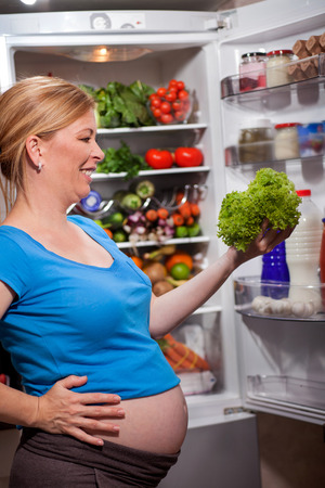 pregnant woman and refrigerator with health food vegetables and fruitsの写真素材