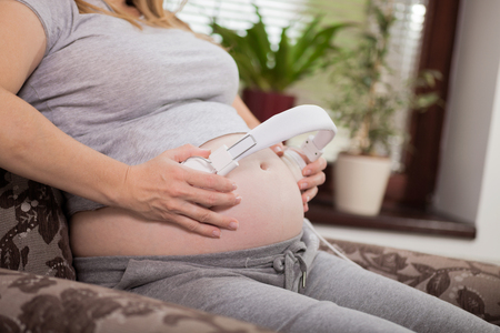 pregnant woman holding headphones on her bellyの写真素材
