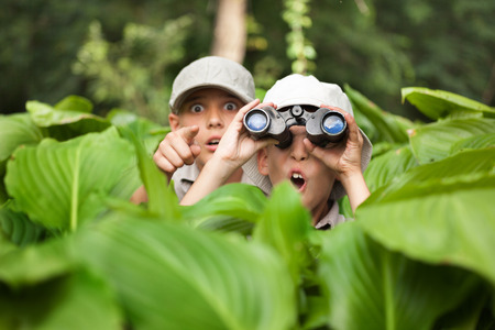 two Boy hiding in grass looking through binoculars outdoor