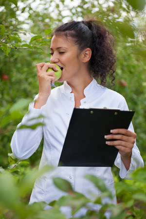 smiling agronomist with notebook standing in apple orchardの写真素材