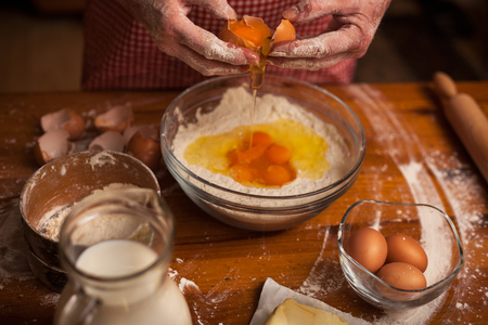 Senior woman hands preparing flour and eggs for cakes or breadの写真素材