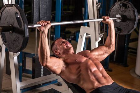 Muscular bodybuilder guy doing exercises with dumbbells in gymの写真素材