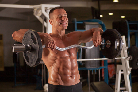 Muscular bodybuilder guy doing exercises with dumbbells in gymの写真素材