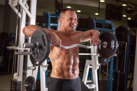 Muscular bodybuilder guy doing exercises with dumbbells in gymの写真素材
