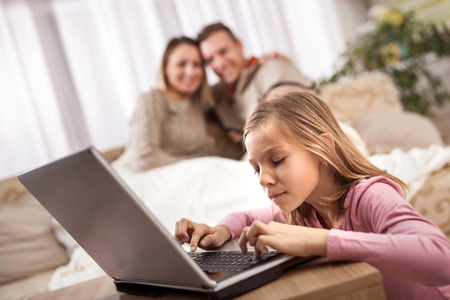smiling girl with tablet pc computer and parents on the back with laptopの写真素材