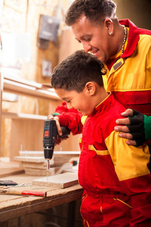 father and little son with drill perforating wood plank at workshopの写真素材