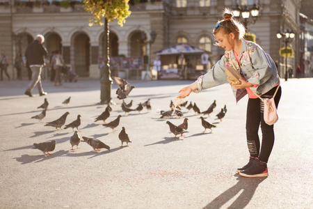 modern young girl feeding pigeons on the city squareの写真素材