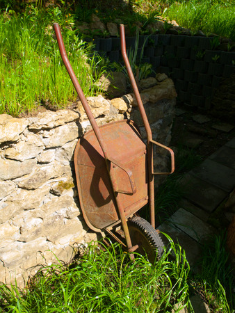 Old rusty garden wheelbarrow leaned on the wall after workの写真素材